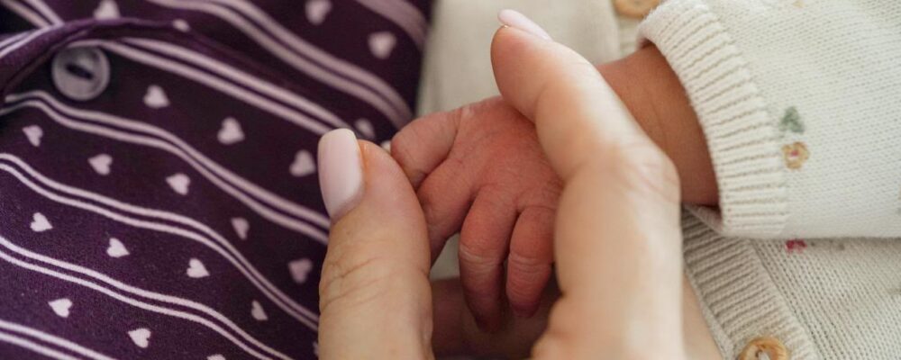 Handje van een pasgeboren baby in de hand van haar moeder