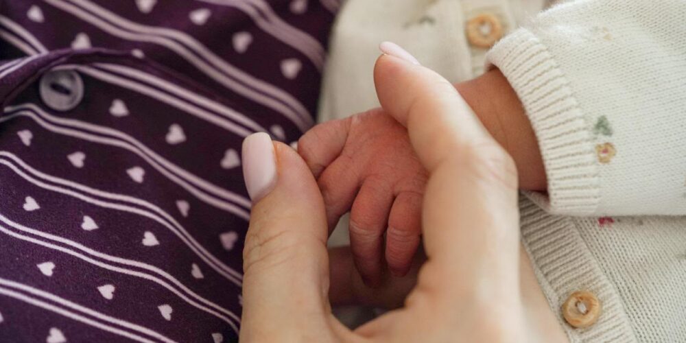 Handje van een pasgeboren baby in de hand van haar moeder