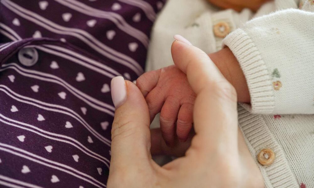 Handje van een pasgeboren baby in de hand van haar moeder
